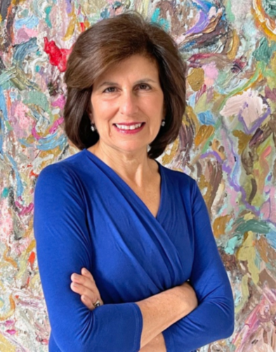 Laurene Sperling, a woman with brown hair wearing a blue long-sleeve top, smiles with arms crossed while standing in front of a colorful abstract painted background.
