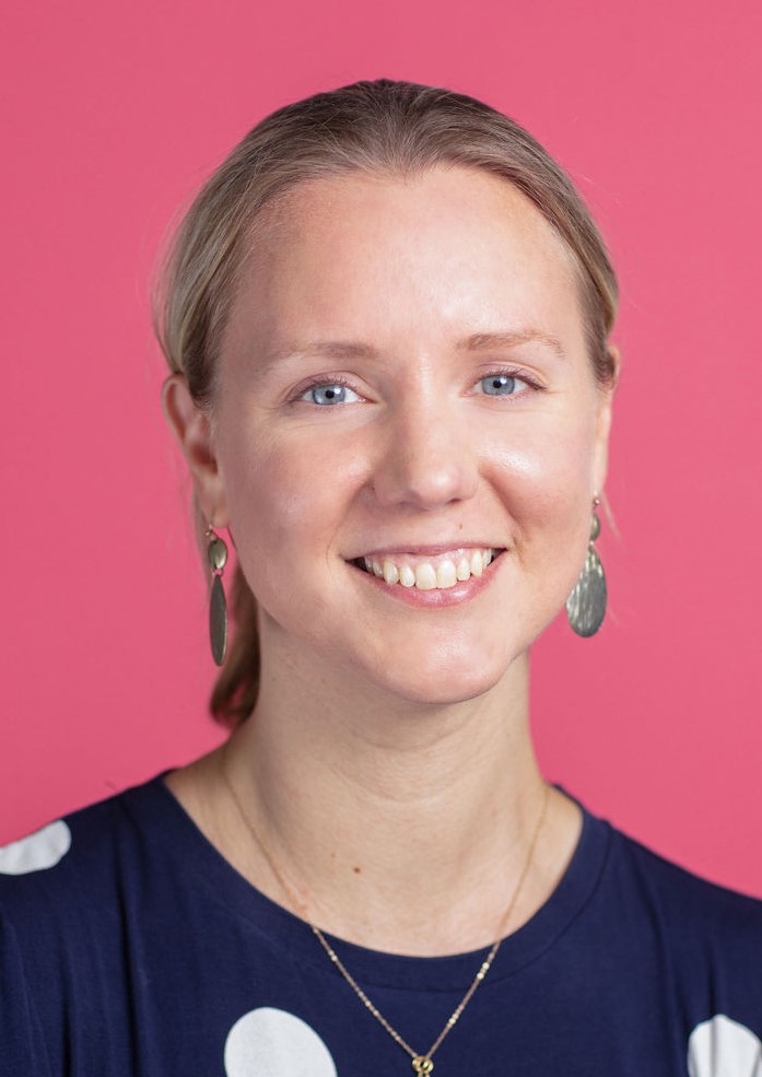A smiling woman wearing a polka dot top and earrings.