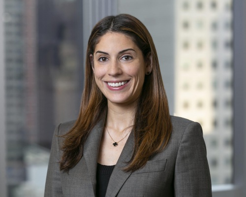 Headshot of Alexa Rachlin wearing a gray suit jacket with city skyline background.