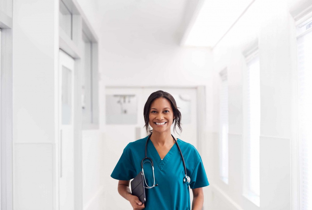 Portrait Of smiling female doctor wearing scrubs In hospital corridor holding digital tablet.