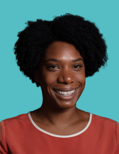 A woman with short curly black hair is smiling, wearing a rust-colored top with a white trim, set against a plain teal background.