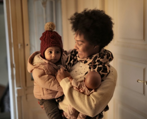 A mother holds her toddler and newborn, both swaddled in winter outfits.