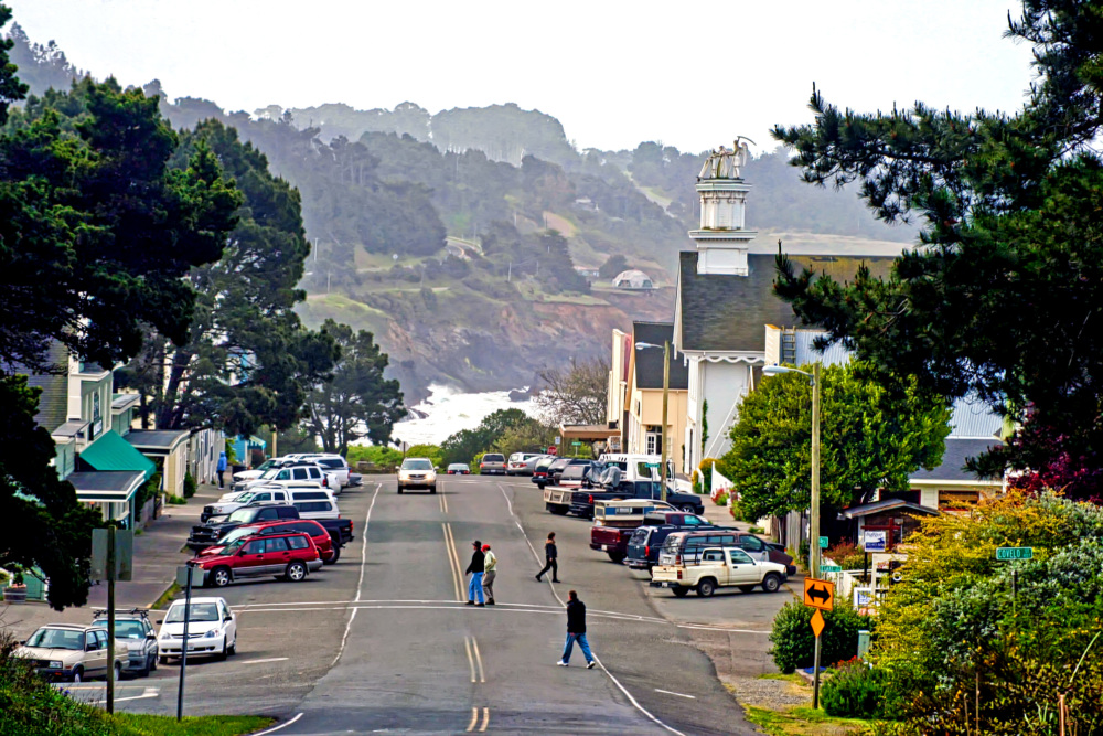 A street with parked cars and a view of the ocean.