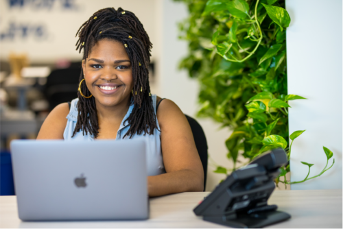 A woman with dreadlocks sitting at a desk with a laptop.