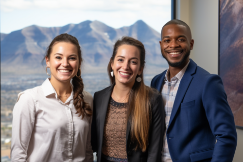 Three students stand and smile in front of a window with mountains behind them