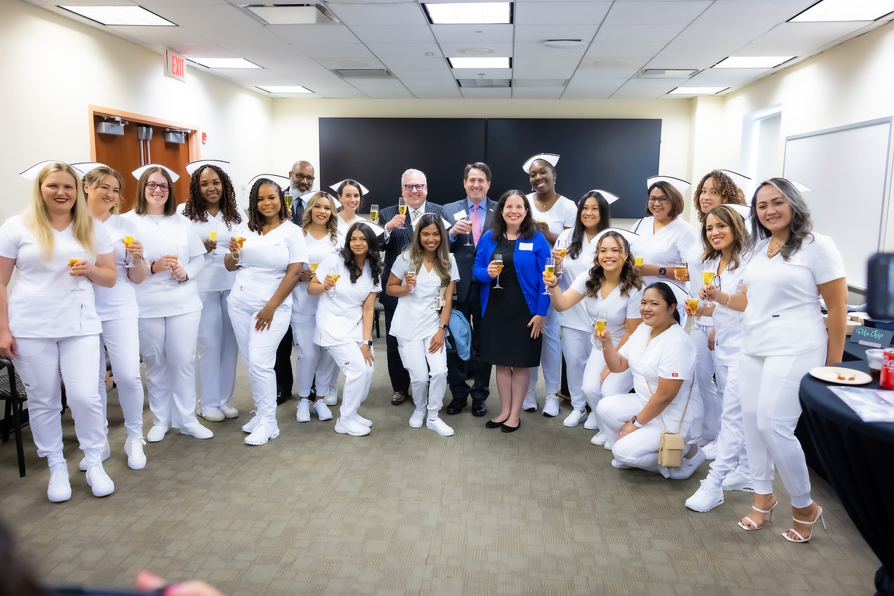 Graduates of HCCC's nursing program stand wearing white nursing outfits beside program funders