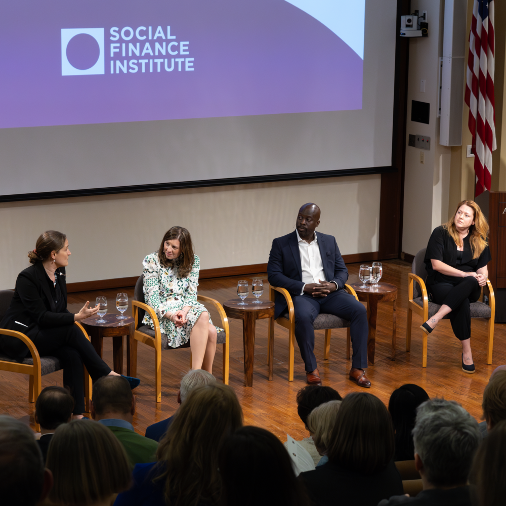 Four panelists are seated on stage in discussion at a Social Finance Institute event, while the audience is seated facing them.