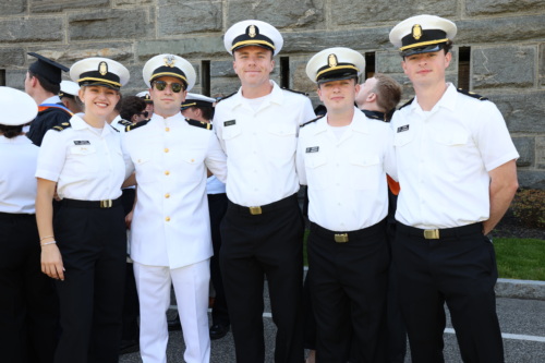 Five people in military attire pose for a group photo in front of a stone wall.