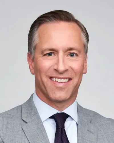 Man in a gray suit and blue shirt, smiling at the camera against a plain background.