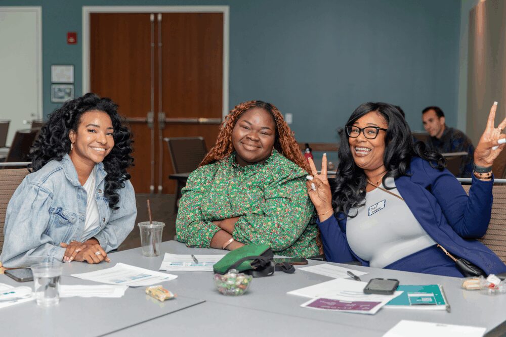 Three Social Finance employees sitting at a table in a conference room smile for the camera