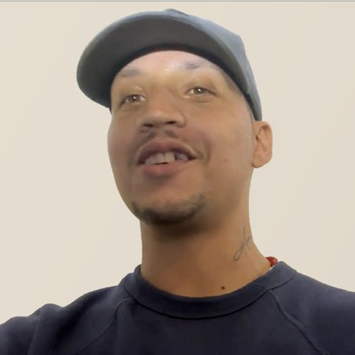 Person wearing a cap and a navy sweatshirt with a logo, smiling and looking away from the camera.