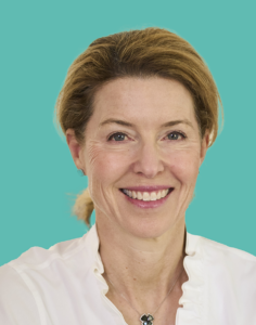 A woman with light brown hair smiling, wearing a white shirt and a necklace, set against a teal background.