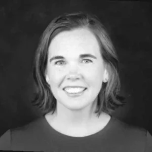 A woman with short hair smiles at the camera against a plain dark background in a black and white portrait.
