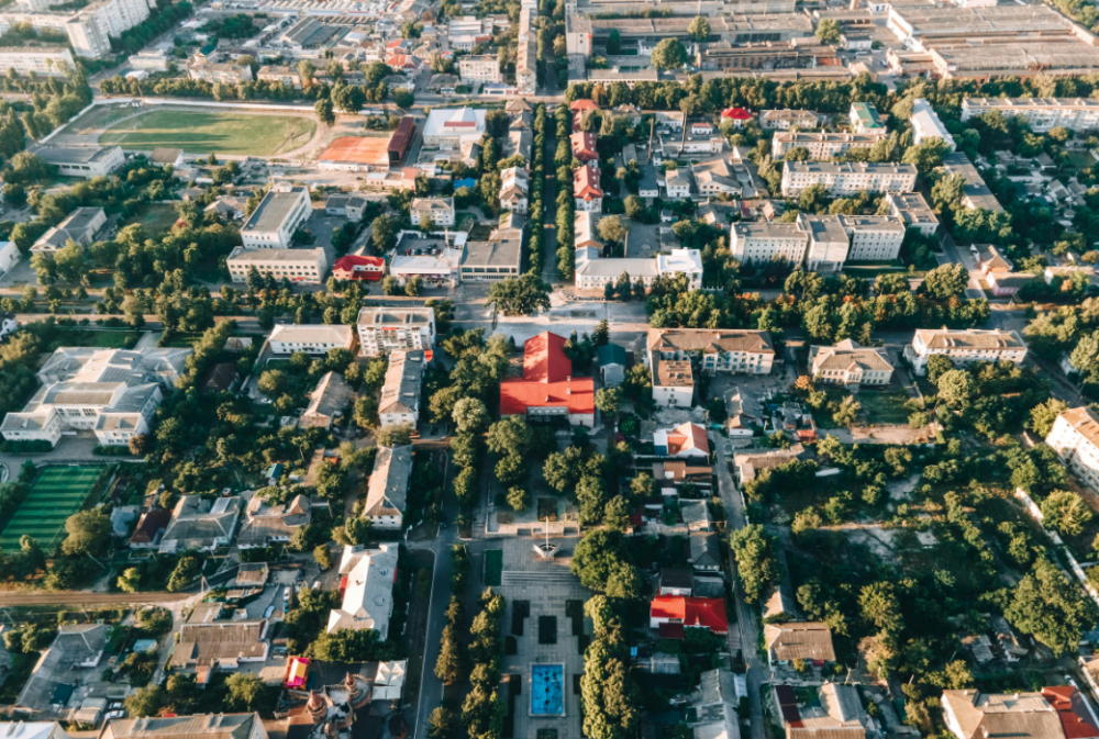 Aerial view of an urban area with tree-lined streets, buildings, and green spaces arranged in a grid pattern.