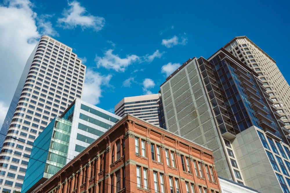Several modern and historic office buildings rise against a blue sky with scattered clouds.