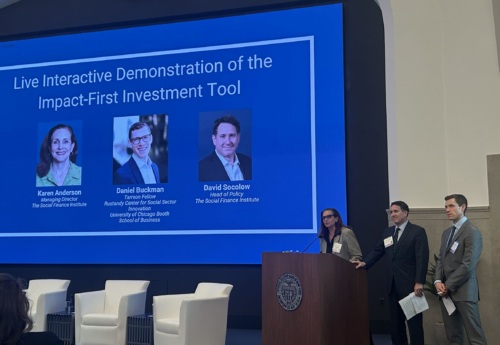 Three people stand at a podium presenting in front of a screen displaying speaker names and photos for a live demonstration of the Impact-First Investment Tool.